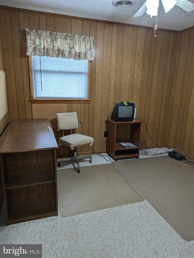 living area featuring wood walls, ceiling fan, and light carpet