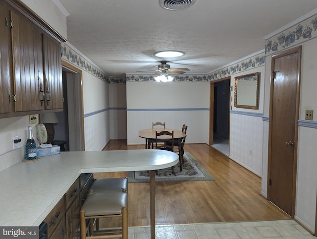 dining space with a wainscoted wall, a textured ceiling, visible vents, ceiling fan, and light wood-style flooring