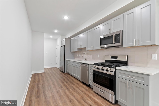 kitchen with stainless steel appliances, light stone counters, sink, backsplash, and light hardwood / wood-style flooring