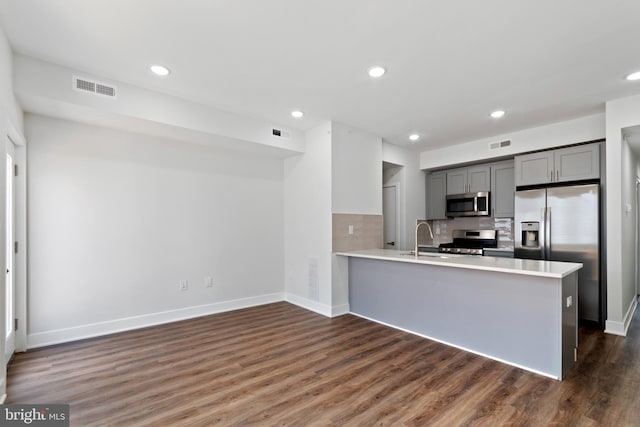 kitchen with dark wood-type flooring, gray cabinetry, kitchen peninsula, and appliances with stainless steel finishes