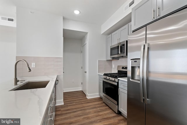 kitchen with light stone counters, stainless steel appliances, dark hardwood / wood-style flooring, decorative backsplash, and sink