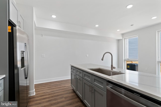 kitchen with stainless steel appliances, light stone counters, sink, gray cabinetry, and dark hardwood / wood-style floors