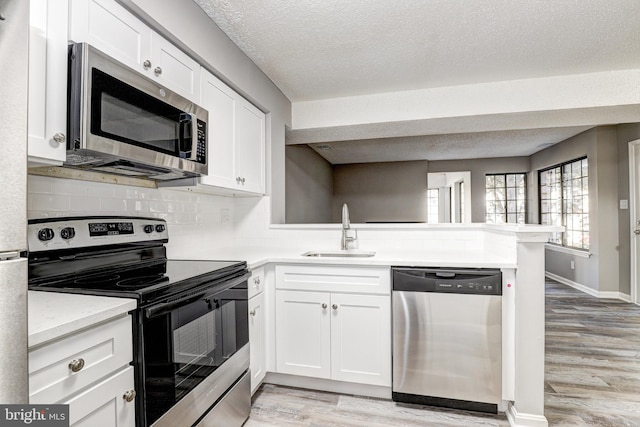 kitchen featuring white cabinets, kitchen peninsula, light hardwood / wood-style flooring, sink, and appliances with stainless steel finishes