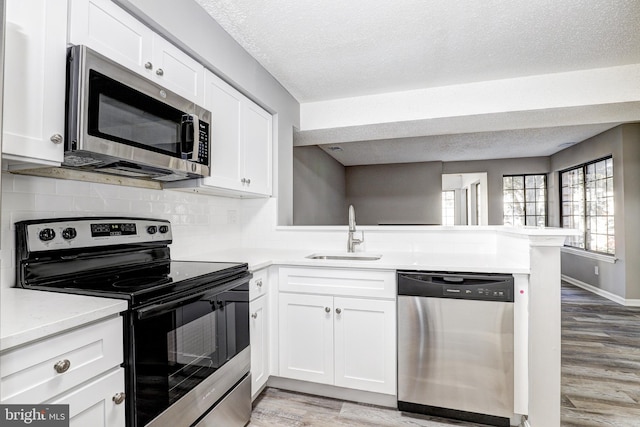 kitchen with stainless steel appliances, sink, light hardwood / wood-style floors, white cabinets, and kitchen peninsula