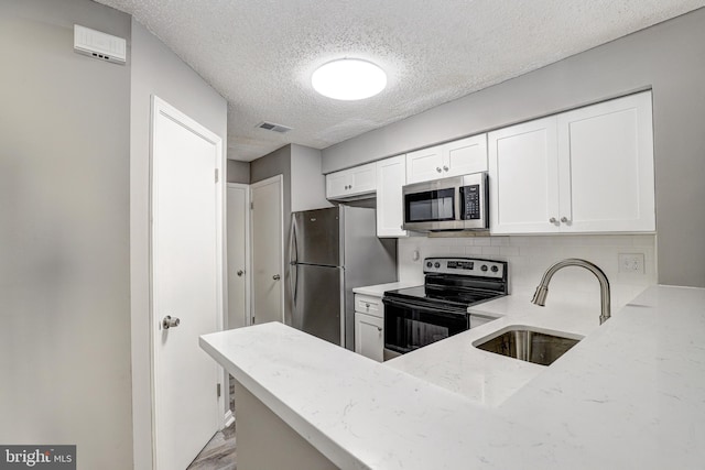 kitchen featuring stainless steel appliances, light stone counters, sink, white cabinetry, and light hardwood / wood-style flooring