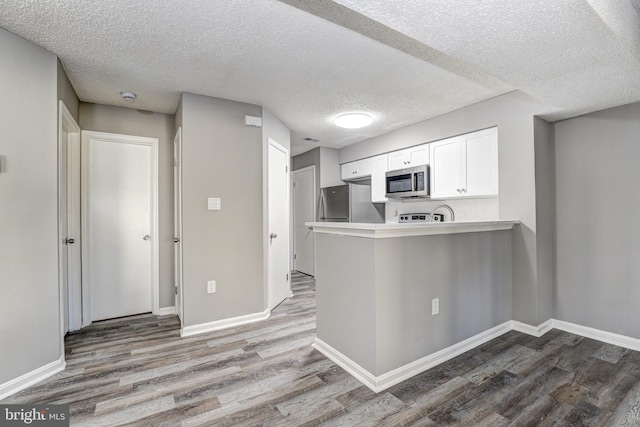 kitchen with light wood-type flooring, kitchen peninsula, appliances with stainless steel finishes, and white cabinets