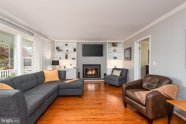 living room with a fireplace, hardwood / wood-style flooring, built in features, and ornamental molding