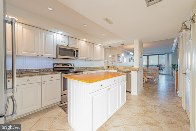 kitchen with light tile patterned flooring, stainless steel appliances, white cabinetry, kitchen peninsula, and a center island