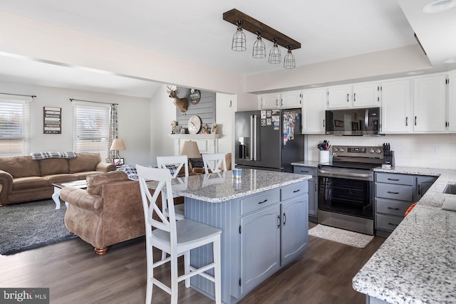 kitchen with stainless steel appliances, a kitchen bar, white cabinets, and dark wood-type flooring