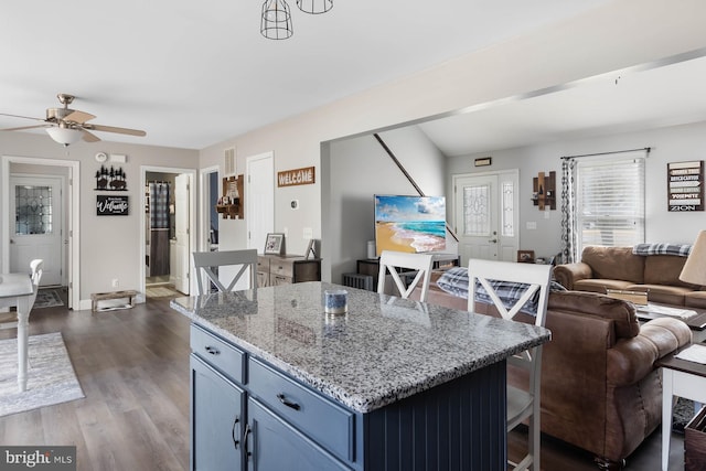 kitchen featuring dark hardwood / wood-style flooring, a center island, blue cabinets, ceiling fan, and light stone countertops