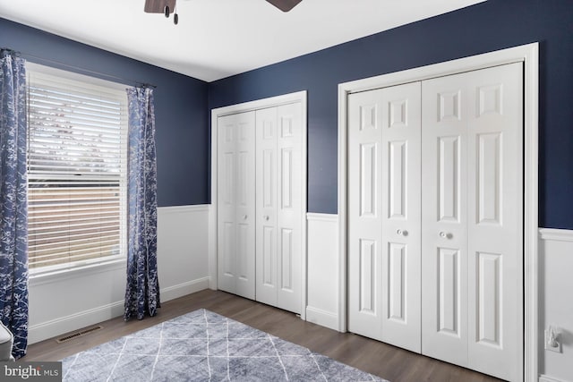 bedroom with wood-type flooring, ceiling fan, and two closets