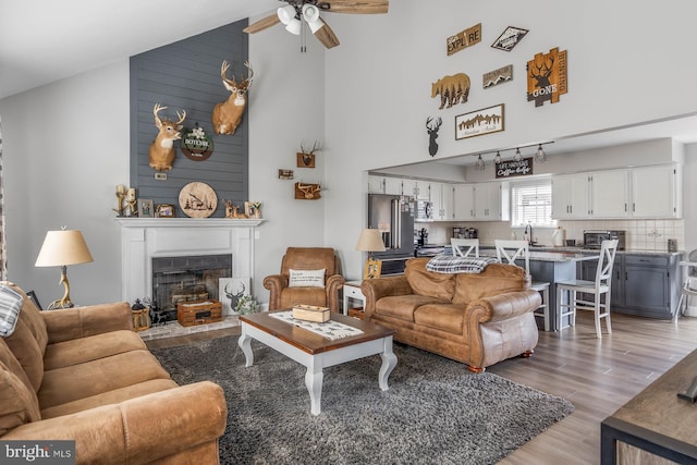 living room with a fireplace, ceiling fan, light wood-type flooring, and high vaulted ceiling