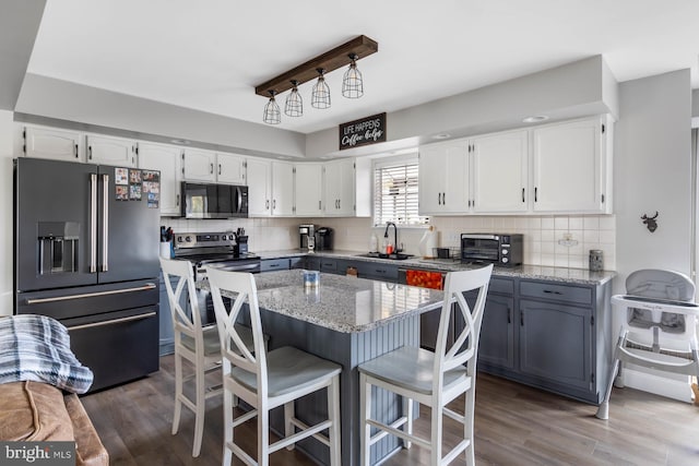 kitchen with white cabinetry, hardwood / wood-style floors, stainless steel appliances, and light stone countertops