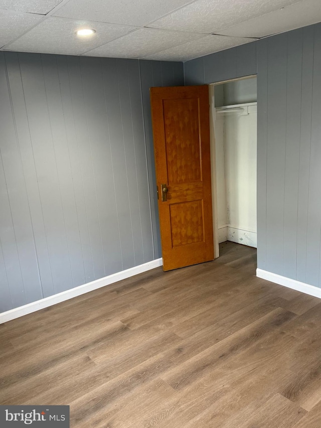 unfurnished bedroom with hardwood / wood-style floors, wood walls, a paneled ceiling, and a closet