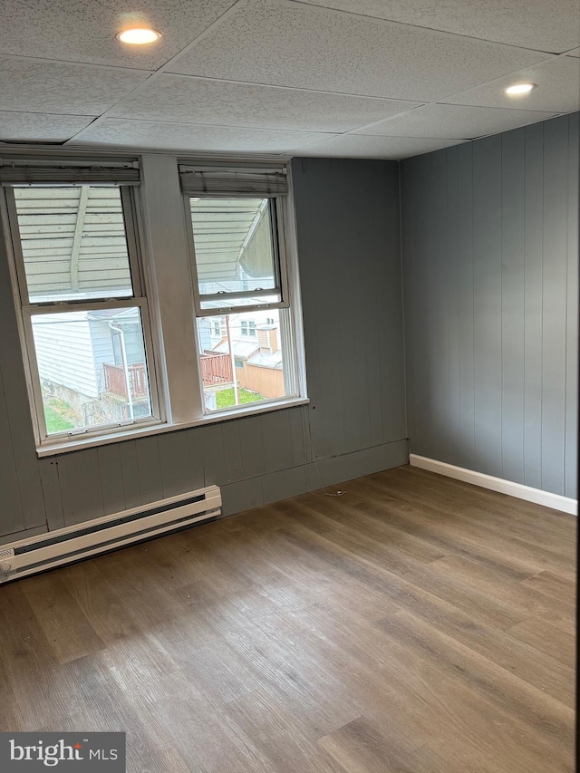 spare room with baseboard heating, a healthy amount of sunlight, a paneled ceiling, and hardwood / wood-style flooring