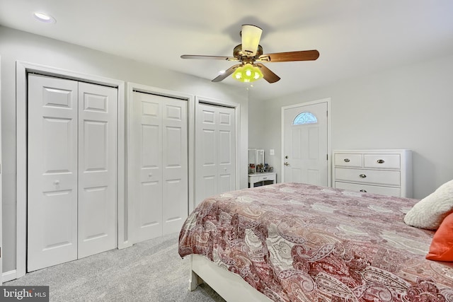 bedroom with two closets, light colored carpet, and ceiling fan