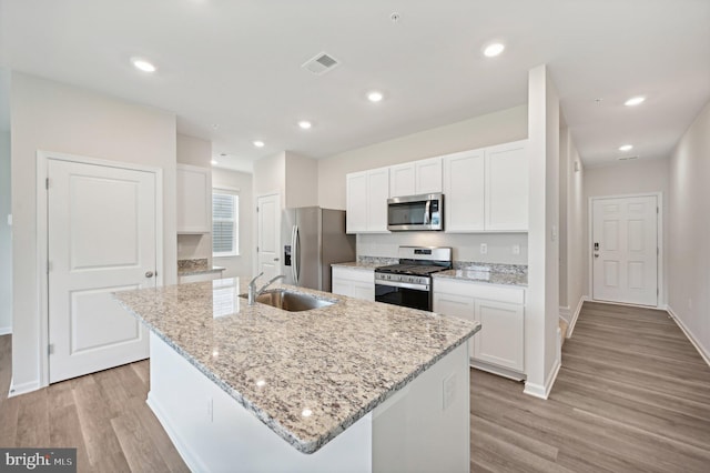 kitchen with white cabinets, stainless steel appliances, sink, and an island with sink