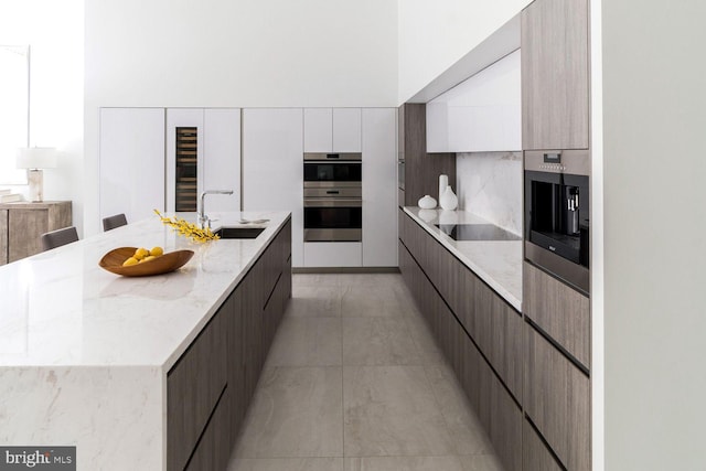 kitchen with white cabinetry, sink, stainless steel double oven, an island with sink, and black electric cooktop