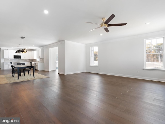 unfurnished living room featuring ceiling fan, dark hardwood / wood-style floors, a healthy amount of sunlight, and ornamental molding