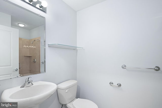 bathroom featuring a tile shower, toilet, and sink