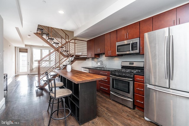 kitchen featuring stainless steel appliances, backsplash, wood counters, a breakfast bar, and dark wood-type flooring