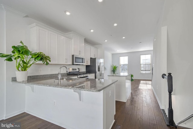 kitchen with sink, a kitchen breakfast bar, kitchen peninsula, white cabinets, and appliances with stainless steel finishes