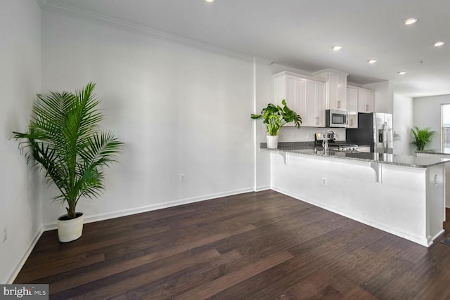 kitchen featuring kitchen peninsula, appliances with stainless steel finishes, white cabinets, and dark stone counters