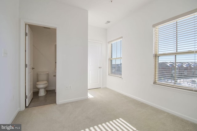 unfurnished bedroom featuring ensuite bathroom and light carpet