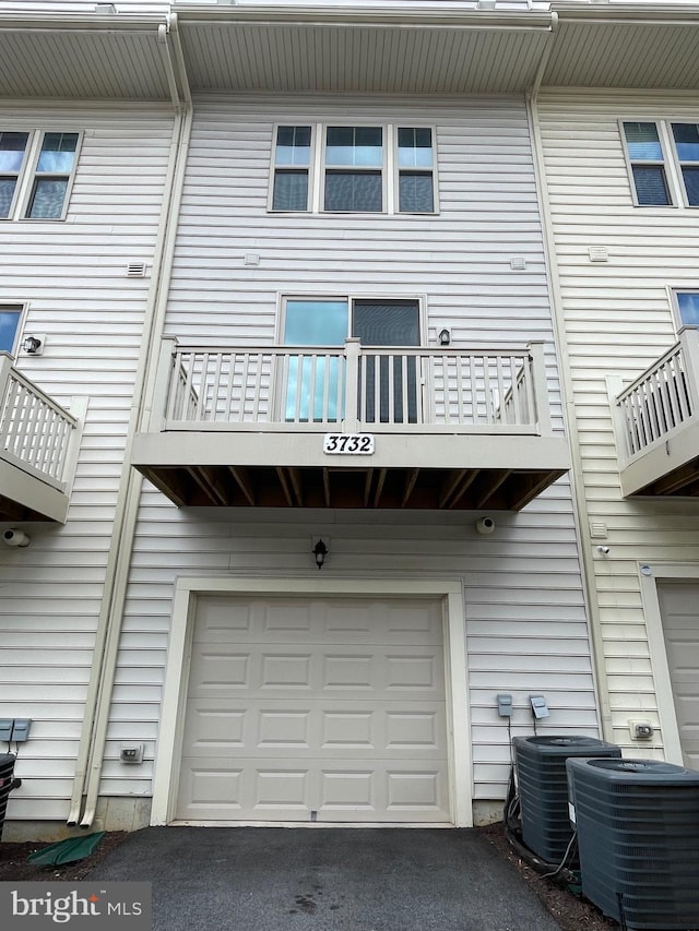 rear view of property featuring a balcony, a garage, and cooling unit