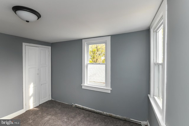 unfurnished bedroom with multiple windows, dark carpet, and a closet