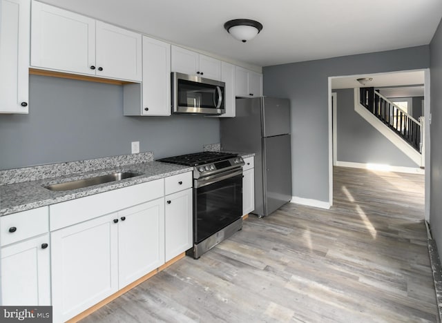 kitchen featuring appliances with stainless steel finishes, light stone countertops, light hardwood / wood-style flooring, and white cabinets