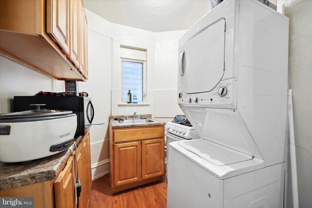 laundry room featuring stacked washing maching and dryer, sink, and light hardwood / wood-style floors