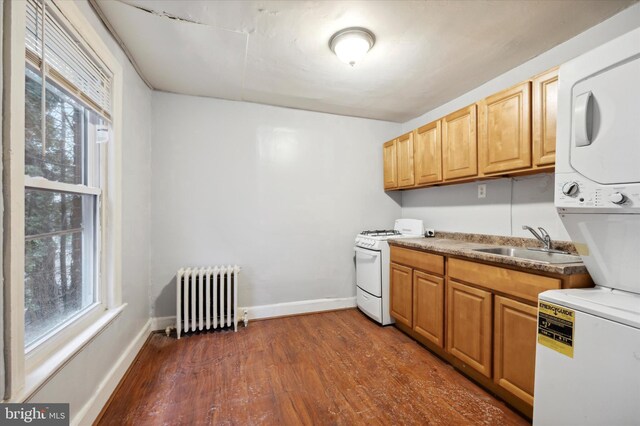 kitchen with stacked washing maching and dryer, a healthy amount of sunlight, white range oven, and radiator