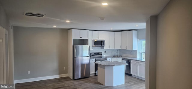 kitchen with a center island, hardwood / wood-style flooring, light stone countertops, white cabinetry, and appliances with stainless steel finishes