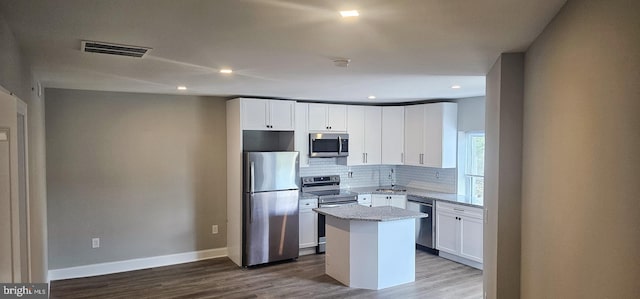 kitchen with stainless steel appliances, wood-type flooring, light stone counters, a center island, and white cabinets