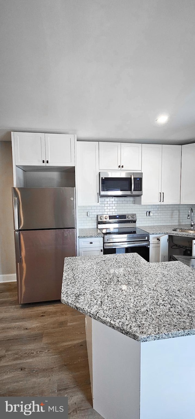 kitchen featuring dark hardwood / wood-style flooring, light stone counters, white cabinets, decorative backsplash, and appliances with stainless steel finishes