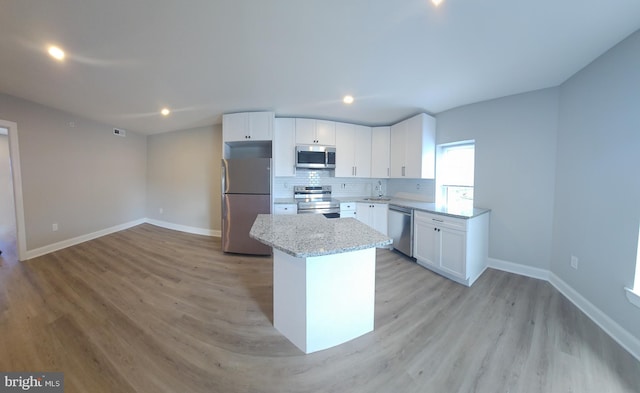 kitchen featuring white cabinetry, light stone counters, appliances with stainless steel finishes, light hardwood / wood-style flooring, and a center island