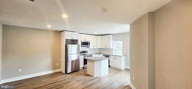 kitchen featuring light stone counters, stainless steel appliances, a center island, white cabinets, and light hardwood / wood-style flooring