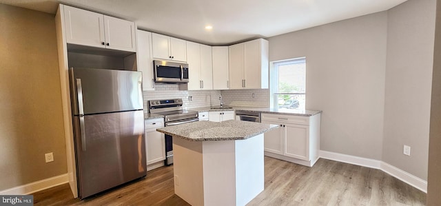 kitchen featuring light stone counters, stainless steel appliances, light wood-type flooring, white cabinets, and a center island