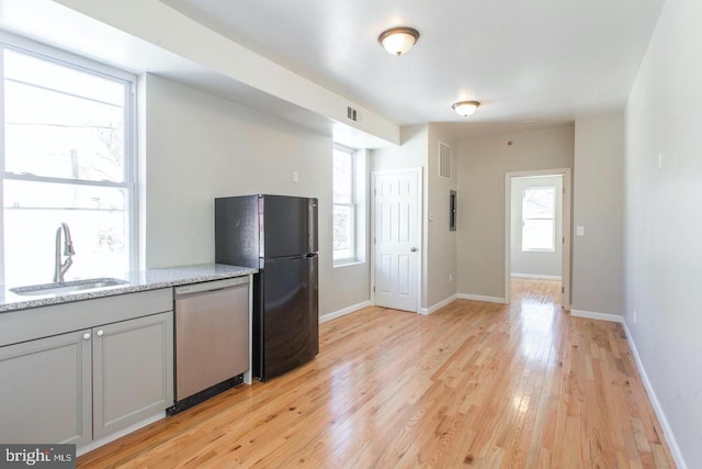 kitchen with sink, stainless steel dishwasher, gray cabinets, black refrigerator, and light wood-type flooring