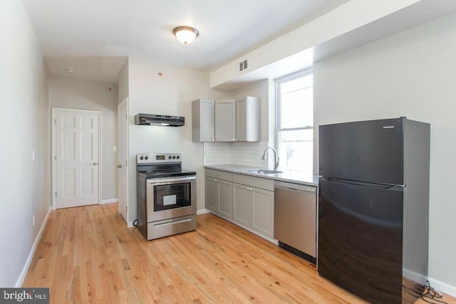 kitchen featuring decorative backsplash, gray cabinetry, light wood-type flooring, appliances with stainless steel finishes, and range hood