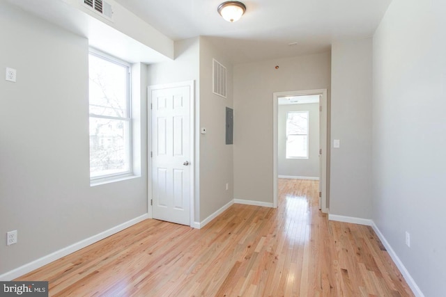 corridor featuring electric panel, a healthy amount of sunlight, and light hardwood / wood-style flooring