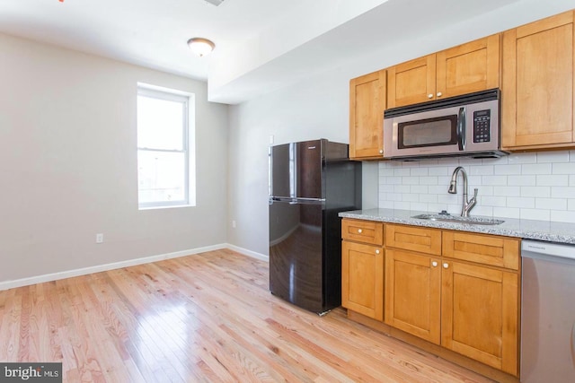 kitchen with light hardwood / wood-style floors, sink, tasteful backsplash, light stone countertops, and appliances with stainless steel finishes