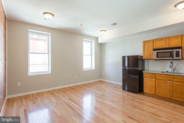 kitchen with black fridge, a wealth of natural light, sink, and light wood-type flooring