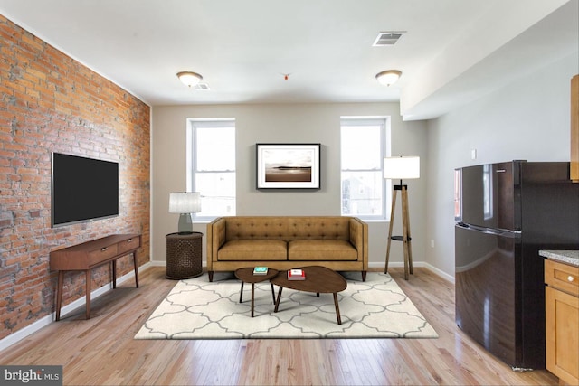 living room with light hardwood / wood-style floors, plenty of natural light, and brick wall