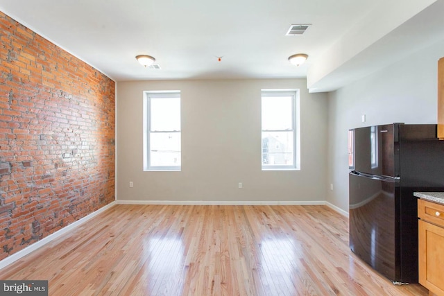 kitchen with light wood-type flooring, black fridge, brick wall, and plenty of natural light