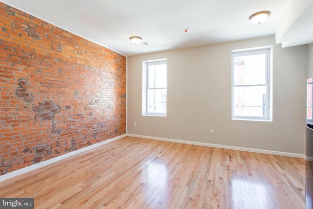 spare room with brick wall and light wood-type flooring