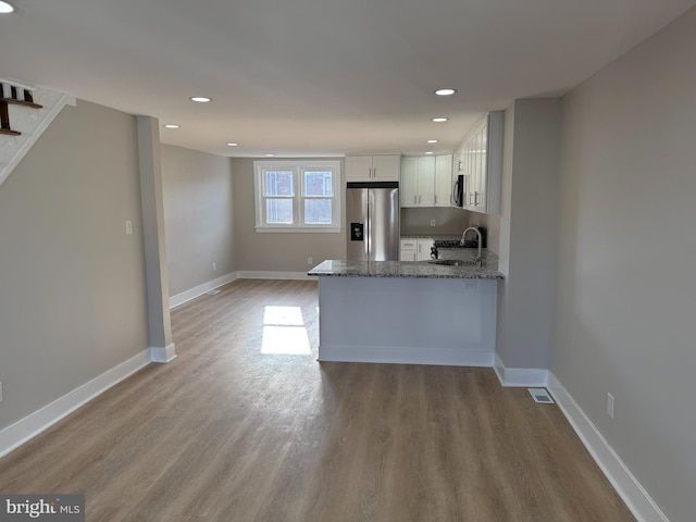 kitchen with stainless steel appliances, white cabinetry, kitchen peninsula, stone counters, and light hardwood / wood-style flooring