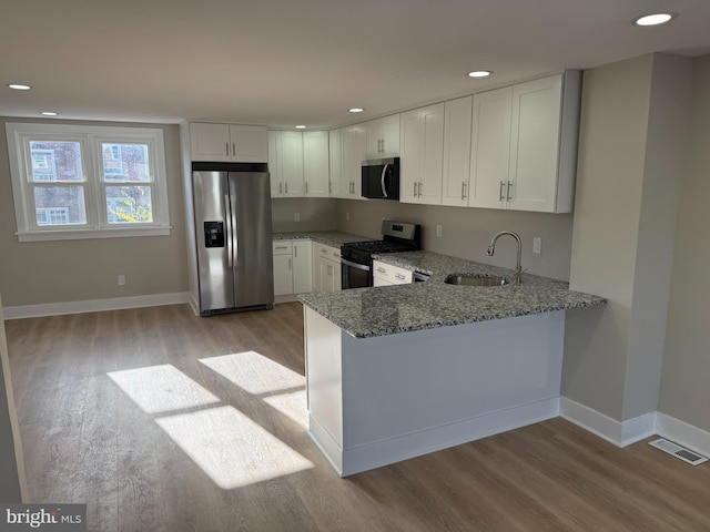 kitchen featuring stainless steel appliances, light hardwood / wood-style floors, sink, kitchen peninsula, and white cabinets