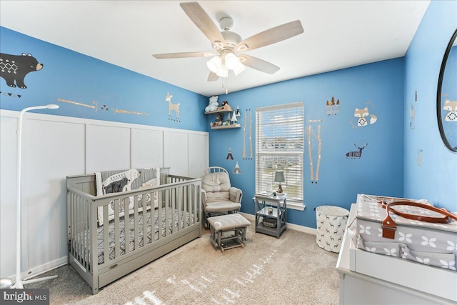 carpeted bedroom featuring ceiling fan and a nursery area